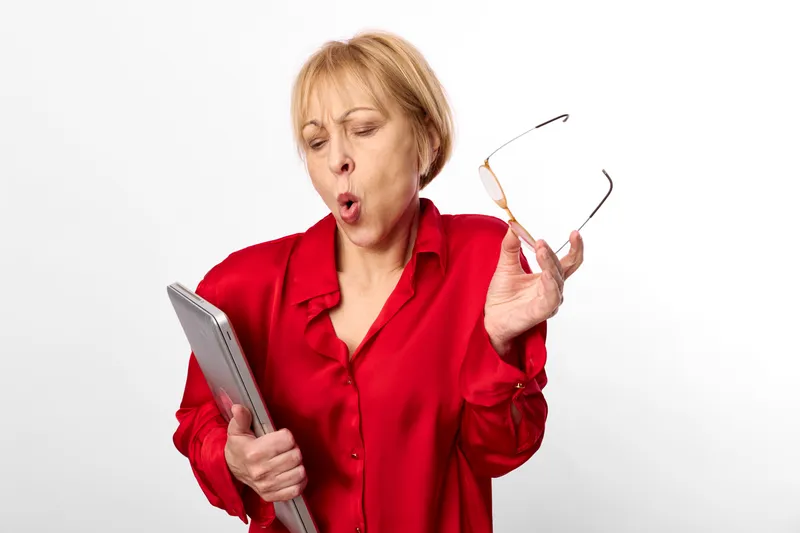 Woman senior surprised holding glasses smartphone tablet, communication technology concept on white studio background, red blouse portrait, indoor hands with tablet and phone, confused