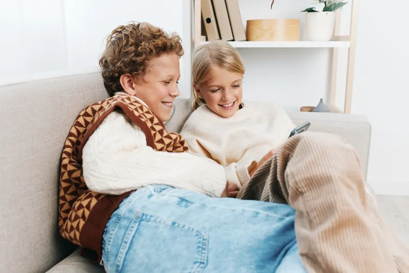 A couple sits close on a cozy sofa, wrapped in sweaters and a blanket, smiling at a tablet. warm, intimate moment highlighting comfort, companionship, and home life.