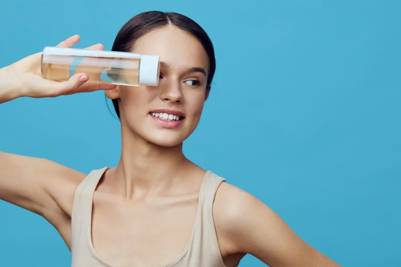 Young female model showcasing a healthy lifestyle with a water bottle on a vivid blue background, evoking freshness and vitality in a summer setting