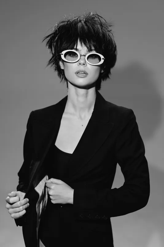 Stylish woman with short hair and sunglasses wearing a black blazer in a black and white portrait.