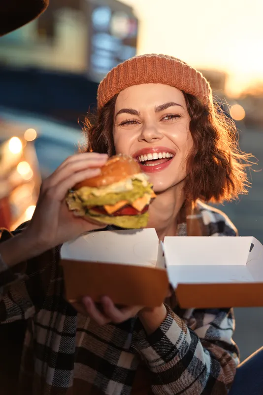 woman burger smile beanie street food box hands: candid lifestyle portrait of a happy female enjoying a takeaway meal in urban golden hour glow, authenticity and emotional storytelling for mindful