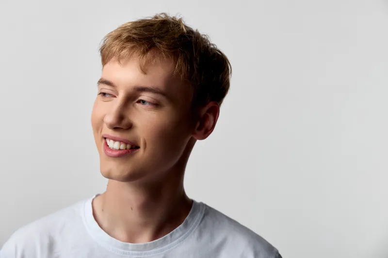 Smiling young man in a white t shirt looks off to the side, conveying warmth, optimism, and relaxed confidence for lifestyle, fashion, and stock photography
