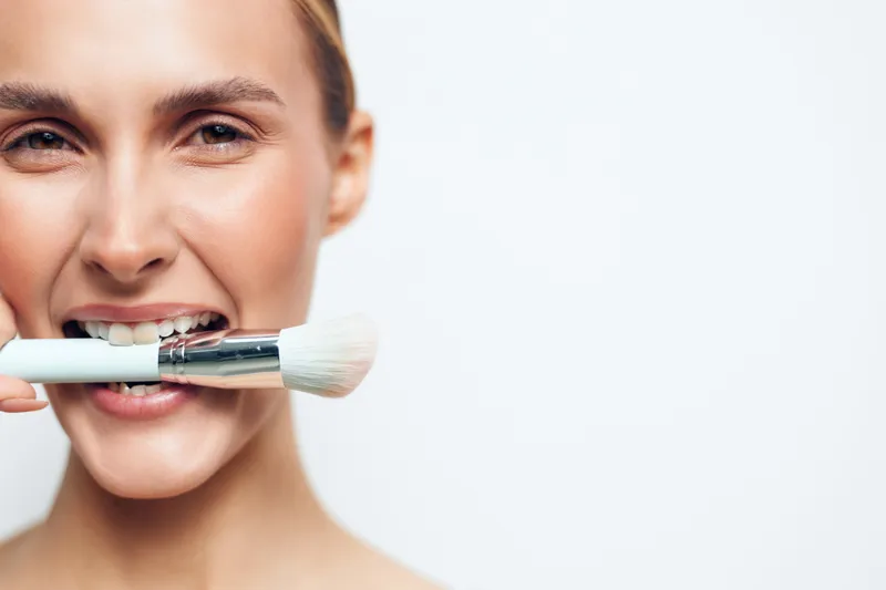 Woman face close up makeup brush, beauty cosmetics on lips, grooming and skincare routine, careful application of foundation, soft light studio background, minimal.