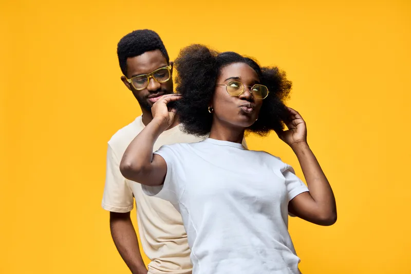 Happy young African couple enjoying playful moments, showcasing natural hair and trendy outfits against a vibrant yellow background