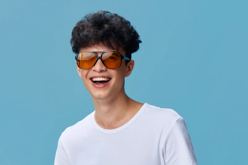smiling man wearing sunglasses and white t-shirt laughing joyfully against blue background, young adult with curly hair, casual style, cheerful mood