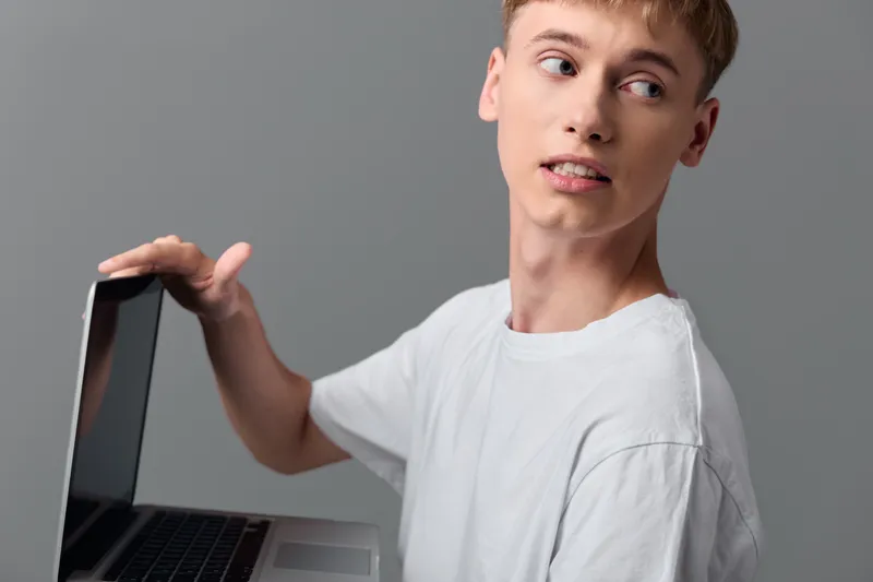 Young man with a laptop in casual setup, looking away from the screen, showcasing learning, remote work and digital communication in a modern studio with a simple background for online learning,