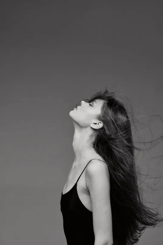 Black and white portrait of a woman with long hair looking up, wearing a black sleeveless top and expressing calm emotion.