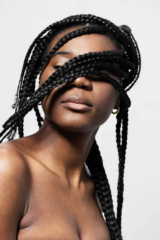 Close up portrait of a young black woman with braided hair covering her eyes, expressing serenity against a minimalist white background