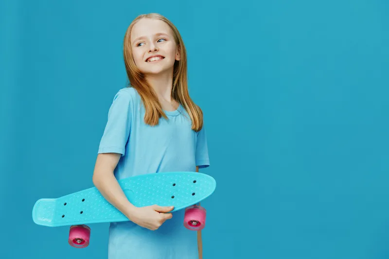 Happy girl with skateboard against a blue background, showcasing youthful joy and a vibrant lifestyle, in casual attire for summer fun