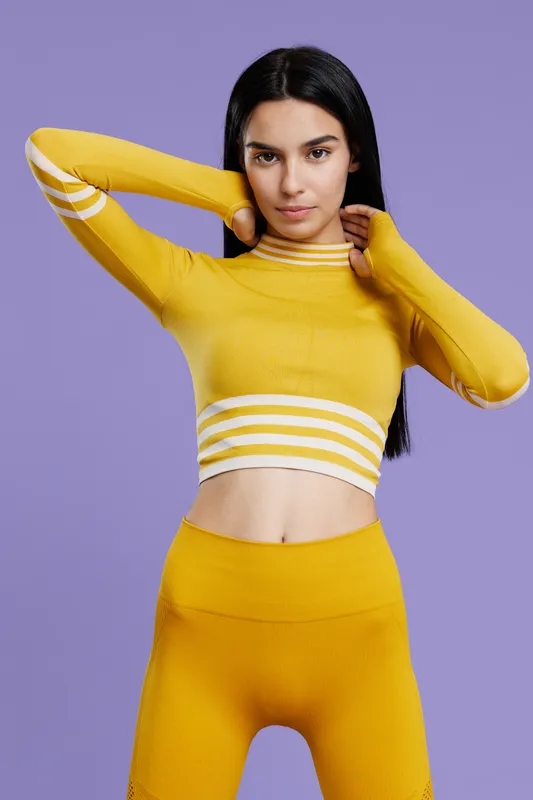 woman sport fitness wearing yellow activewear posing against purple background with focused expression, long dark hair, and modern minimal style.