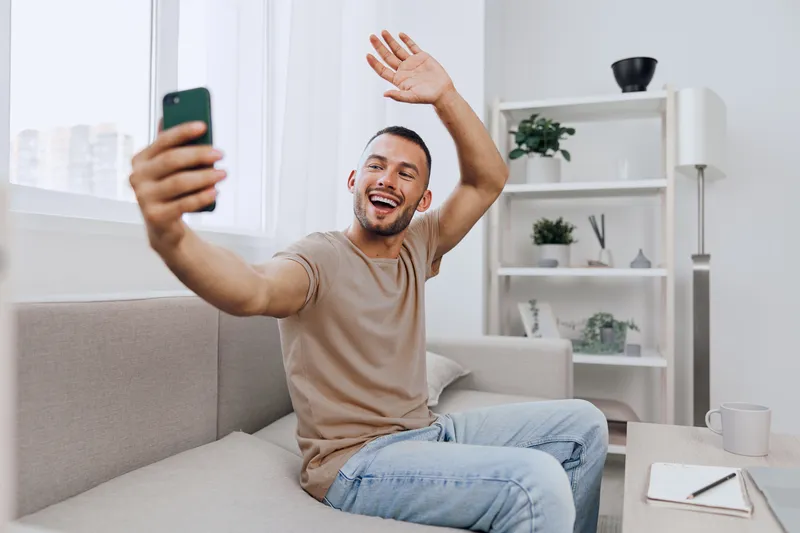 A happy man engaging in a video call, reflecting soft masculinity and emotional connections while practicing digital detox at home.