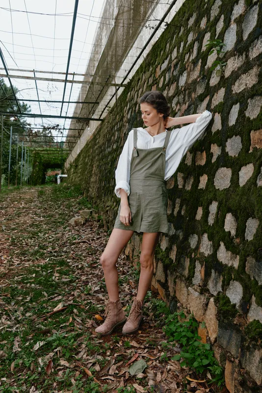 Young woman in casual summer outfit stands against a moss covered wall, showcasing a relaxed vibe and connection to nature Perfect for lifestyle and fashion shoots