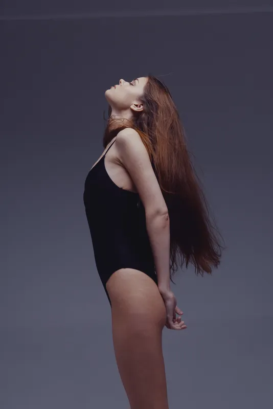 woman stretching in black bodysuit with long hair on gray background, fitness, flexibility, posture