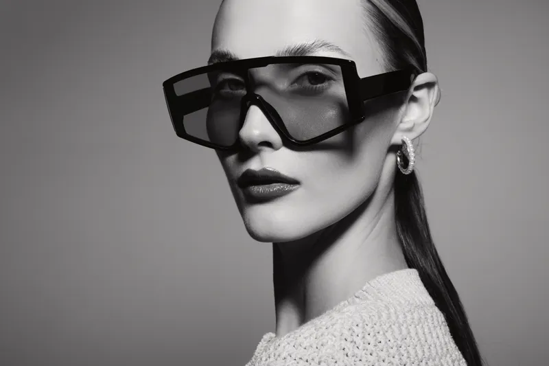 Portrait of a fair skinned Caucasian woman wearing oversized sunglasses and elegant earrings against grey background.