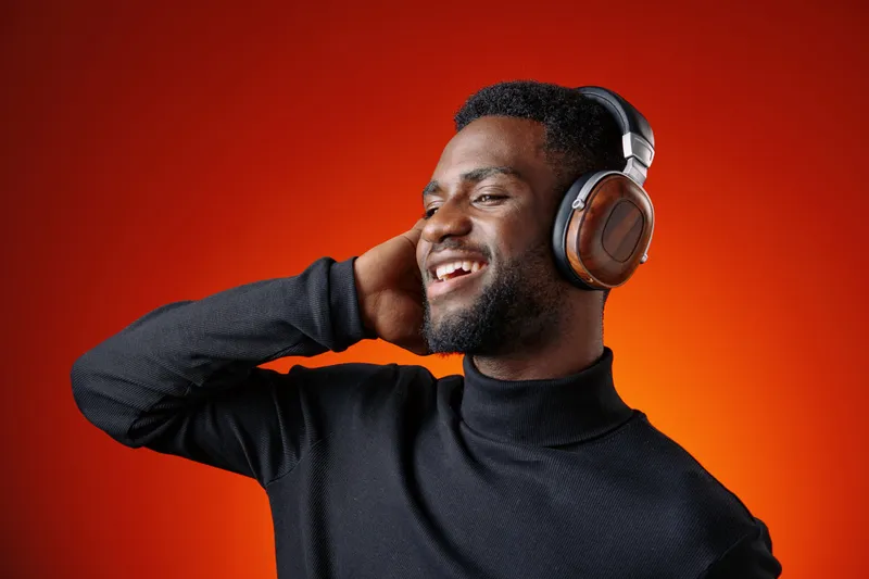 Young Black man enjoying music with headphones against an orange background, smiling with happiness and confidence Music, headphones, joy, vibrant colors, portrait, lifestyle