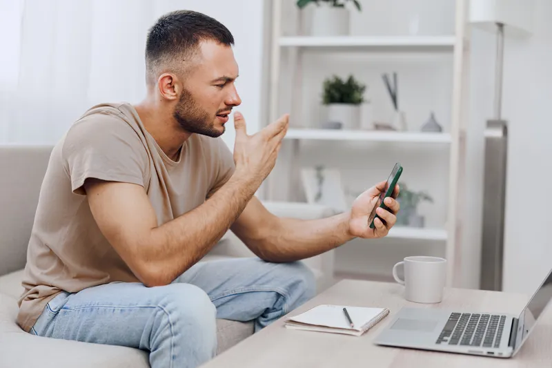 Engaged man communicating on a video call while sitting at home, displaying curiosity and emotion, surrounded by a modern interior design.