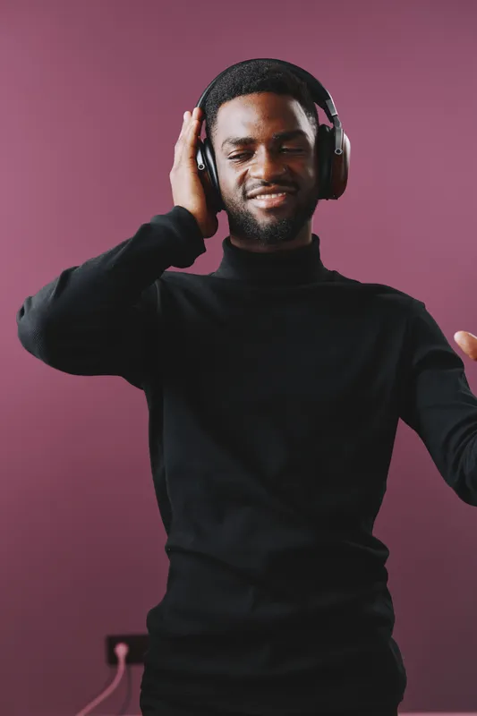 Young Black man enjoying music with headphones in a cozy, modern setting, wearing a black sweater, expressing joy and relaxation