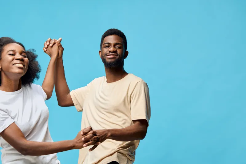 Happy young couple dancing together against a bright blue background, expressing joy and love through playful interactions in casual clothing