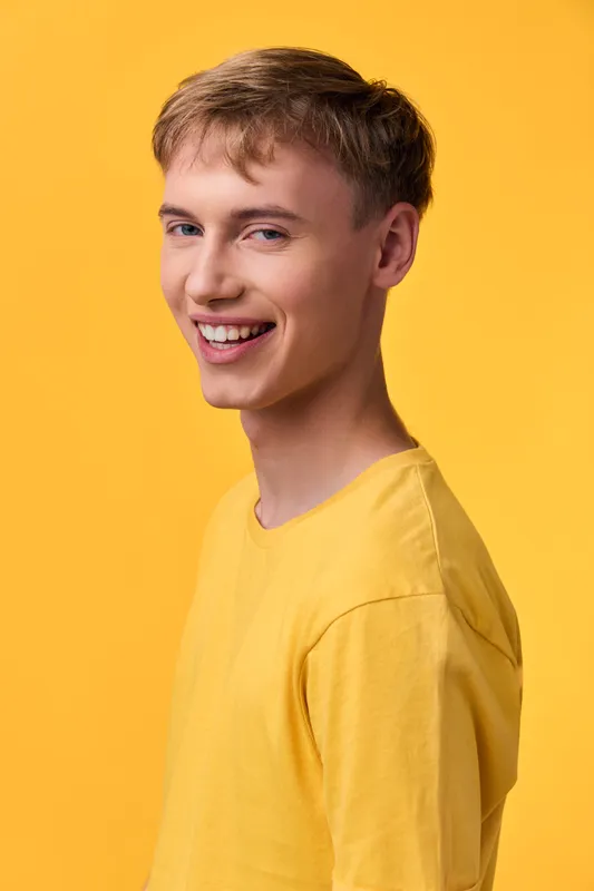 Smiling man in a yellow shirt stands against a bright yellow background, conveying happiness and approachability. A warm casual lifestyle shot suitable for marketing, fashion, and corporate