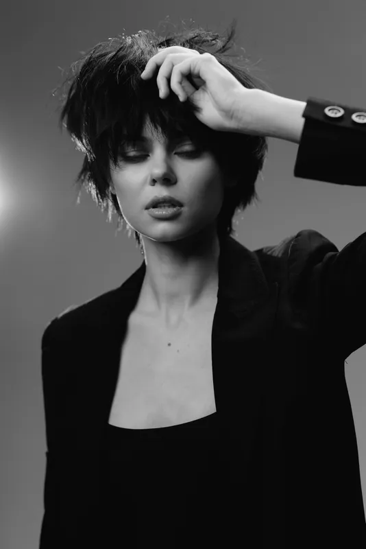 Black and white portrait of a young woman with short hair in a thoughtful pose wearing a dark blazer and top.