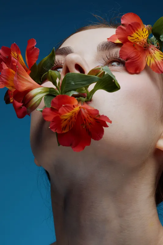 Close up portrait of a female model with red flowers, expressing serenity and beauty against a blue background, perfect for concepts of nature and wellness