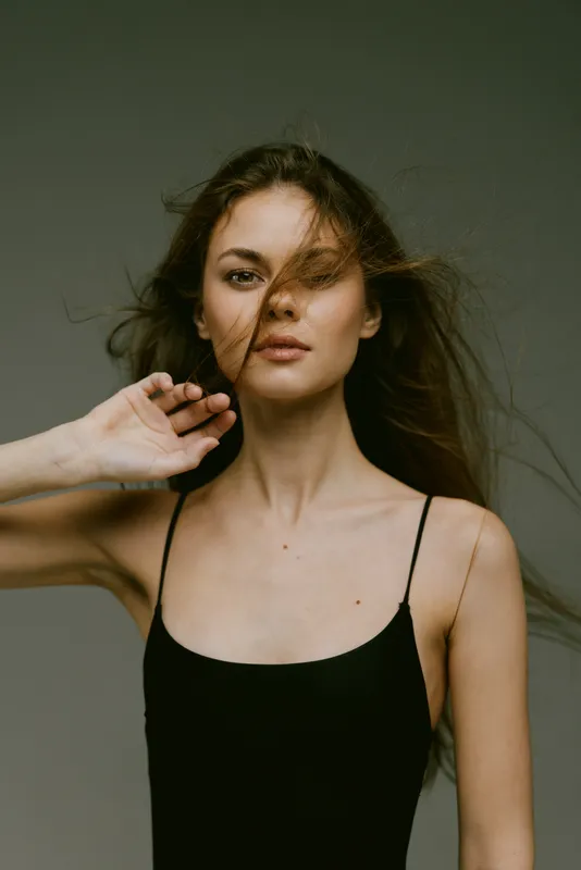 young woman with flowing hair in black tank top with neutral expression in studio lighting