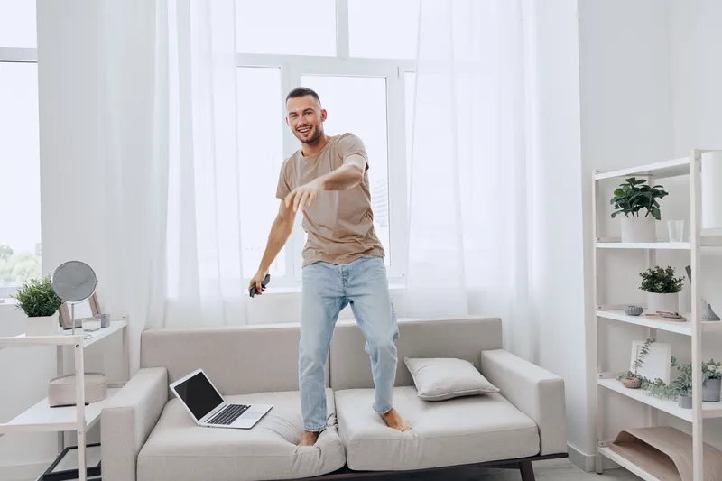 Happy man dancing at home, embracing life’s imperfections while managing work-life balance and digital detox in a cozy, bright living space.