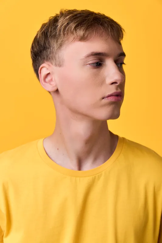 Youthful male in a yellow tee shown in side profile against a warm studio backdrop, casual style, calm mood, and contemporary minimalism for lifestyle branding