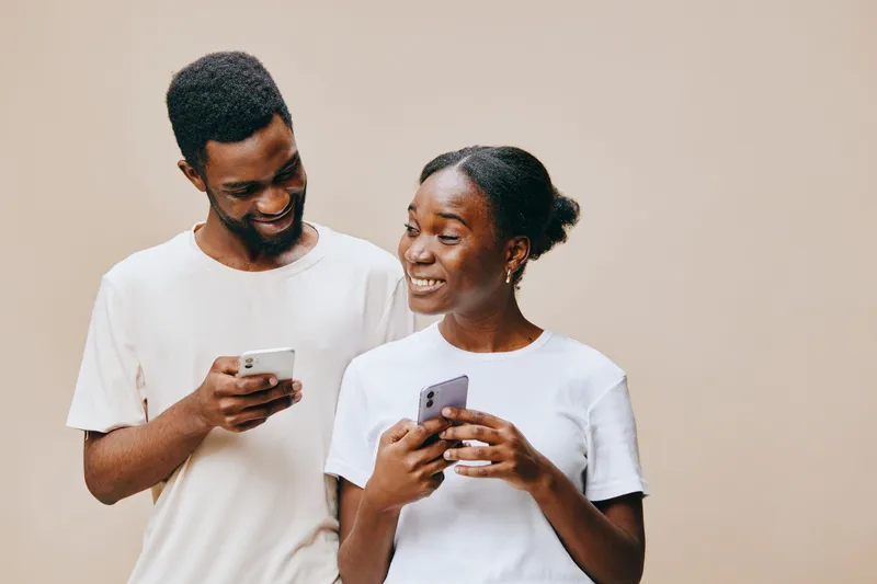Happy young couple using smartphones together, wearing casual white t shirts, showcasing joy and connection against a neutral background