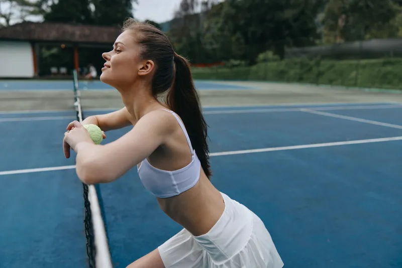 Young athletic woman in sportswear enjoying a moment after a tennis match, showcasing determination and joy on a sunny day on a blue tennis court