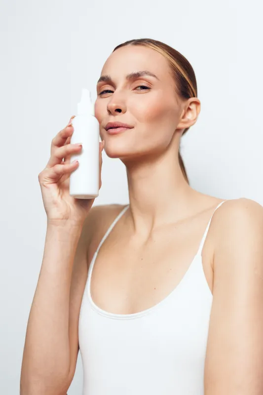 Woman skincare serum moisturizer beauty hygiene treatment spa portrait confidence, she applies serum to her face, gentle smile, clean white background, routine concept for hydration