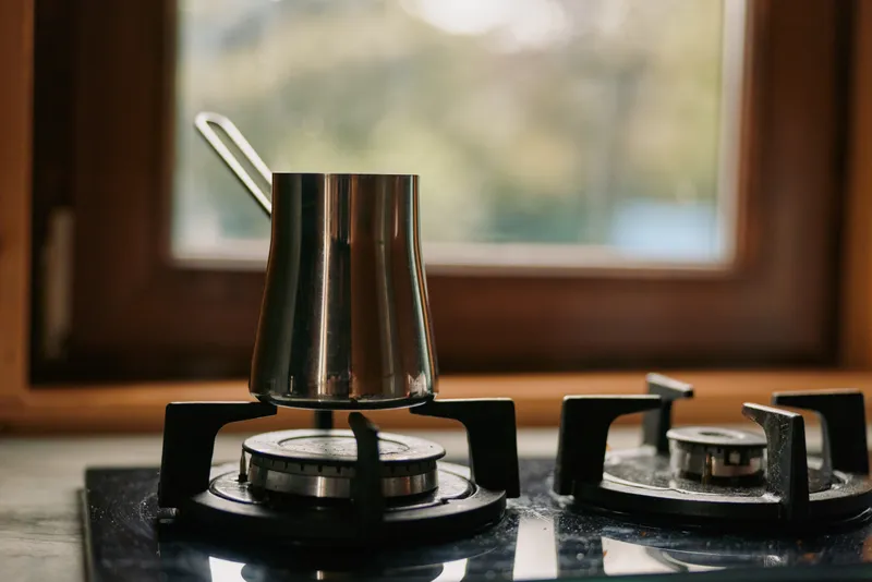 Coffee cezve stove kitchen pot gas brewing window authenticity inclusivity metal closeup morning rustic scene of traditional coffee preparation with steam and warm light