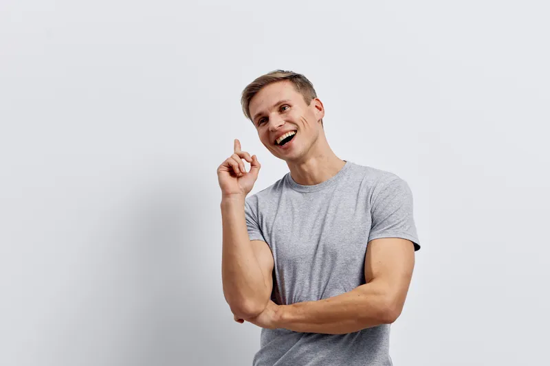 smiling young man wearing grey t-shirt pointing up look camera digital detox concept white background studio portrait