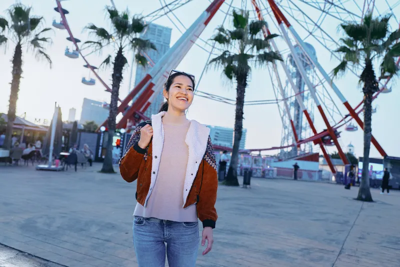 Woman, smiling, outdoor, urban, fashion, casual, travel, scenery, plaza, amusement in cityscape with palm trees and ferris wheel, daylight, street style, candid moment, lifestyle