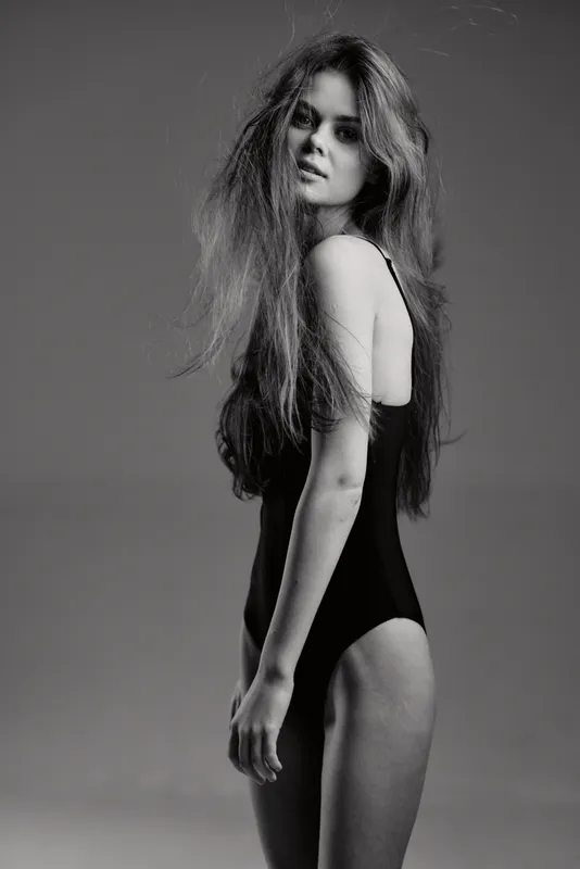 Black and white portrait of a tall woman with long hair wearing a black bodysuit with serious expression