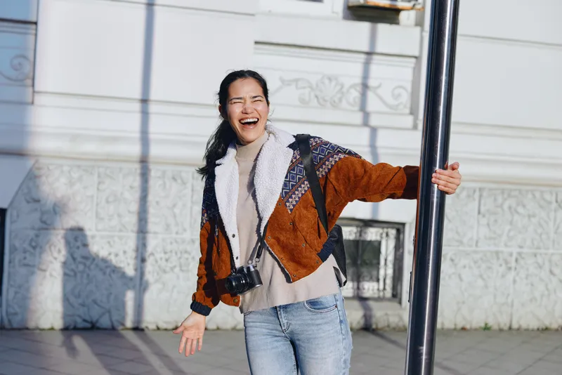 laughter outdoors street camera casual fashion happiness candid moment as a joyful figure enjoys a sunny day beside a tall pole on the sidewalk