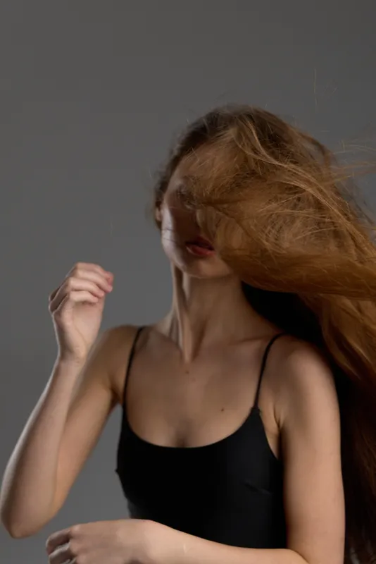 Woman with flowing hair wearing black top, capturing motion and natural beauty in soft lighting.