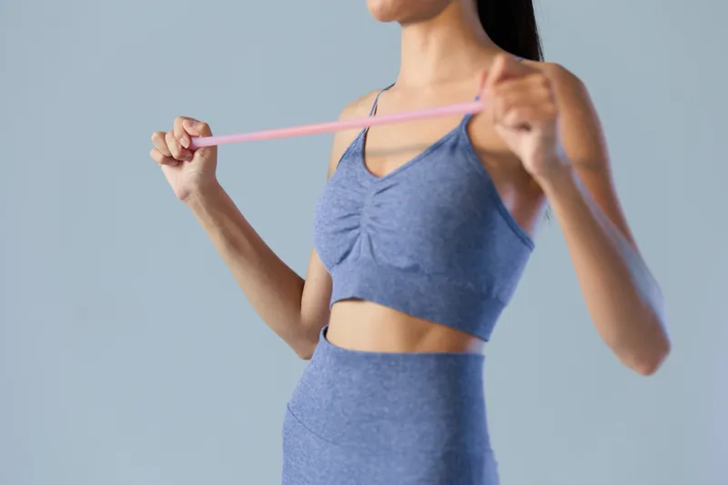 woman sport fitness wearing blue workout outfit using pink resistance band for strength training in indoor studio with simple gray background