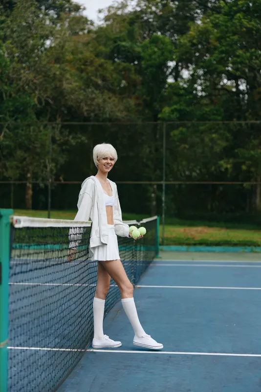 Stylish young female tennis player in sporty outfit smiling on the court, showcasing healthy lifestyle and active lifestyle concept