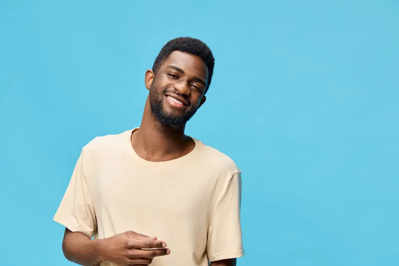 Young smiling African American man wearing a casual beige t shirt against a bright blue background, representing happiness and confidence in a vibrant lifestyle