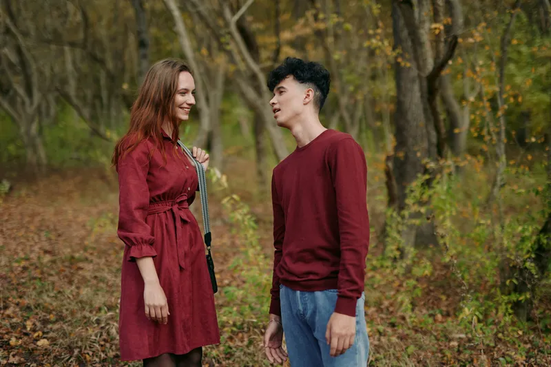 A candid outdoor portrait of a young couple in autumn woods, capturing authentic interaction and genuine expressions; natural lighting emphasizes relaxed posture, real smiles and quiet connection.
