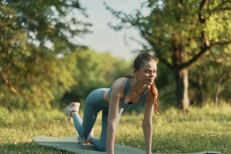 Fit young woman practicing yoga outdoors in a lush green park, wearing a comfortable blue outfit, exuding tranquility and focus during her exercise routine