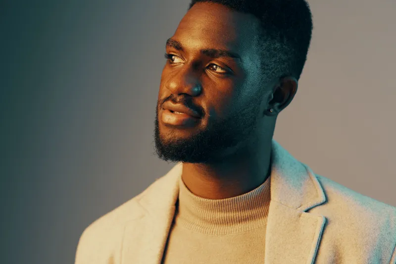 Thoughtful young Black man in a stylish blazer, expressing calm emotions with a soft smile against a gradient background, perfect for lifestyle and fashion themes