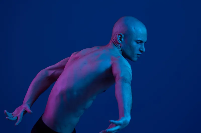 Dynamic athletic man in a blue background, showcasing graceful motion and strength. The image highlights his toned physique and powerful expression.