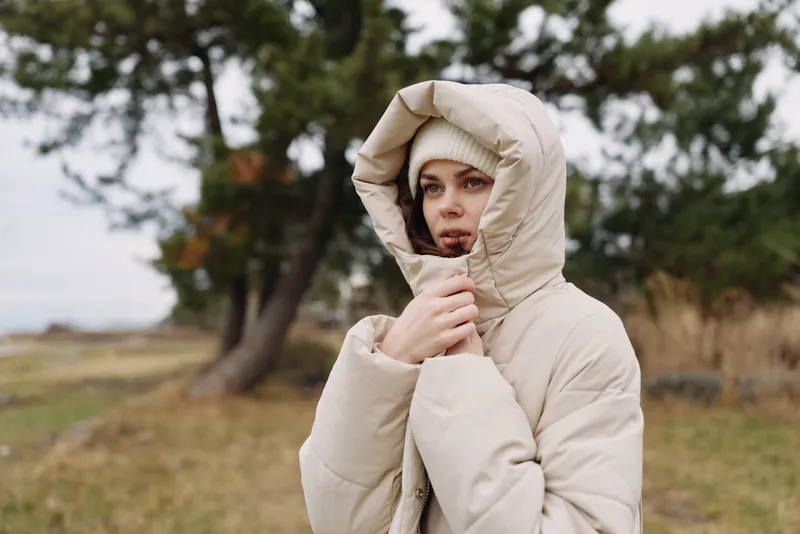Person outdoor jacket hood portrait autumn beige coat in a field with trees and grass, a calm solitary mood with soft natural light, nature scene and season atmosphere