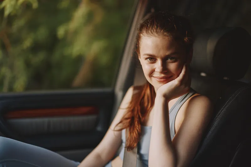 Young woman smiling in the car with a relaxed expression, wearing casual sportswear, showcasing a natural outdoor background and warm lighting