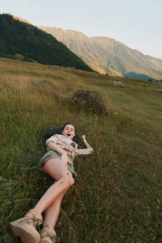 Young woman lying on grass in a mountain meadow, wearing casual clothes and boots, enjoying nature and outdoor lifestyle during daytime.