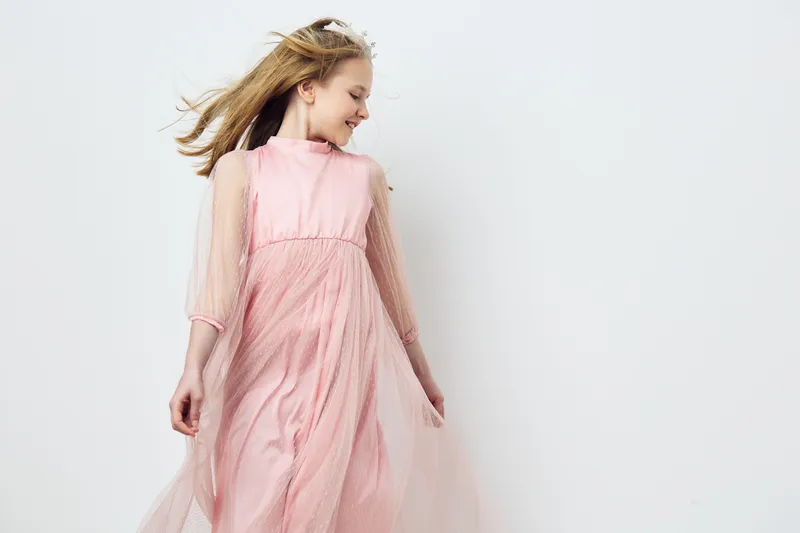 Young girl in a flowing pink dress, smiling joyfully against a light background, embodying innocence and carefree spirit, perfect for spring and summer themes