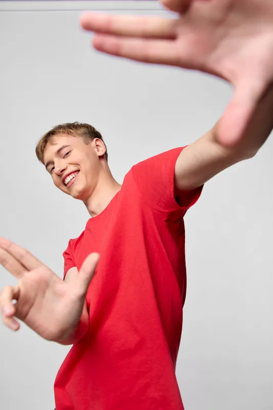 Dynamic shot of a smiling youth reaching toward the camera in a bright red shirt, conveying energy, playfulness and action for lifestyle, youth, and marketing visuals
