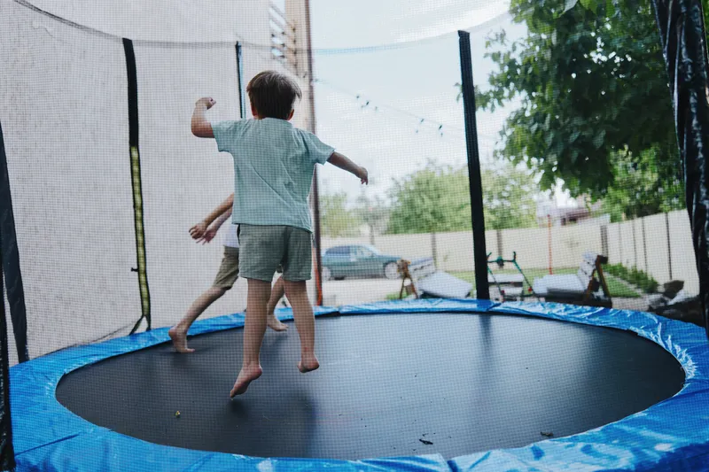 Joyful boy jumping on a trampoline, enjoying the sunny day. The vibrant outdoor setting creates a lively atmosphere full of energy and playfulness.